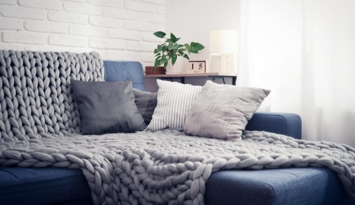 Gray knitted blanket from merino wool on couch with pillows in the interior of the living room